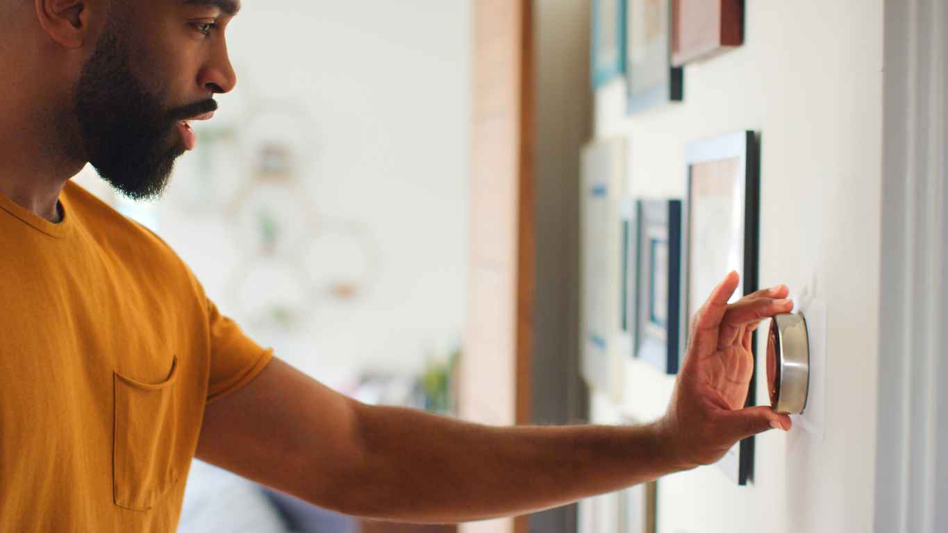 Close Up Of Man Adjusting Heating Thermostat Control In Room