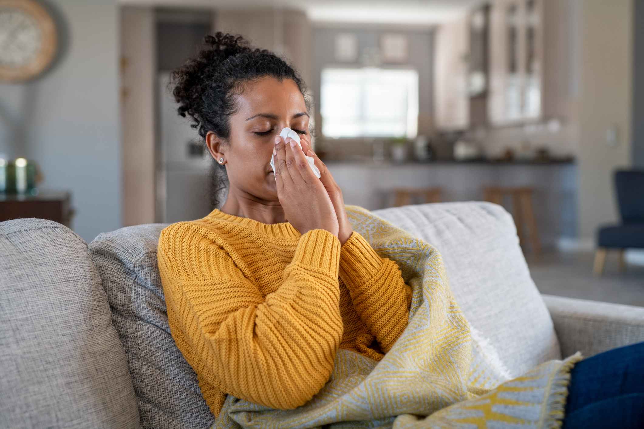 Young woman sneezing into a tissue on her sofa due to fall allergies