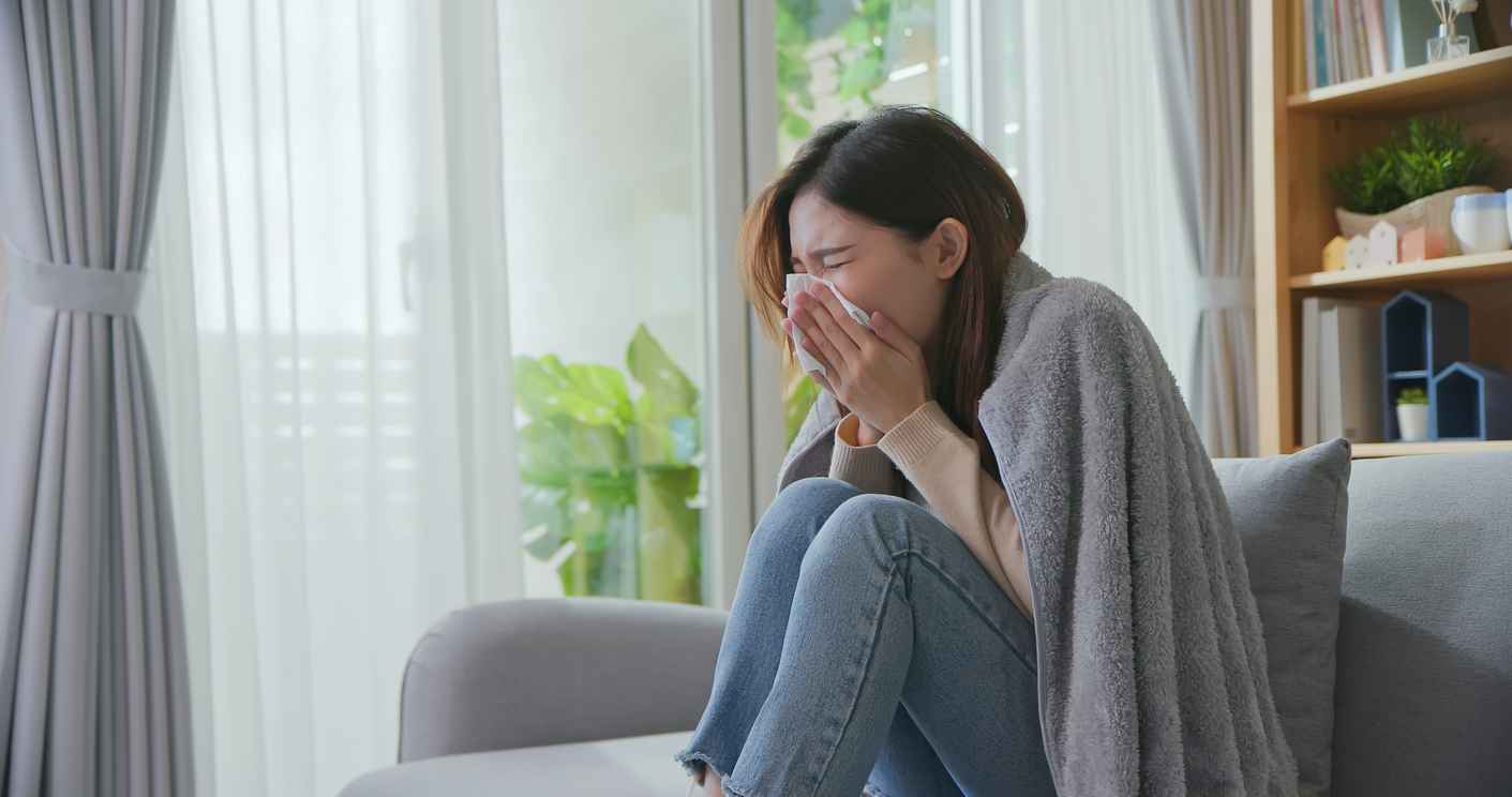 A woman sitting on her sofa sneezing into a tissue because of allergies