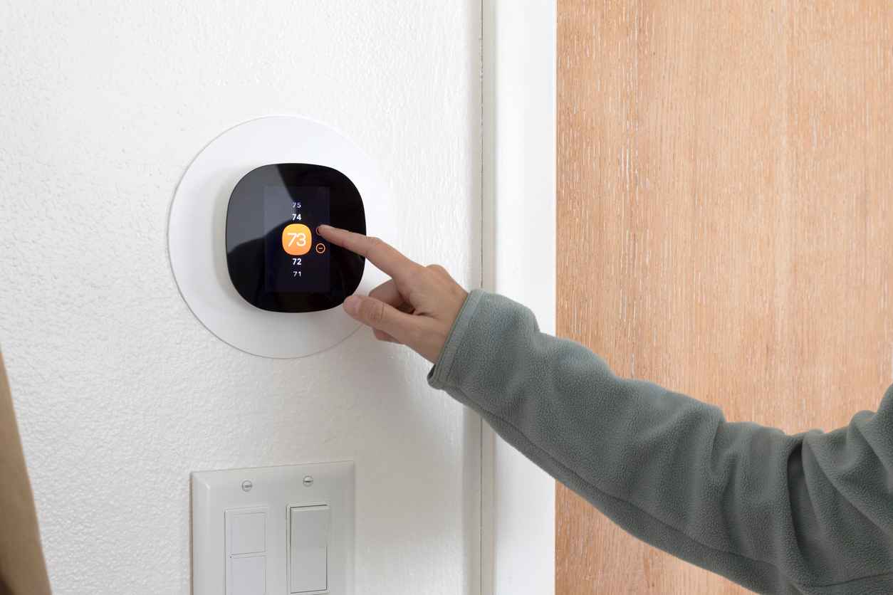 A person using a smart thermostat to increase the room temperature