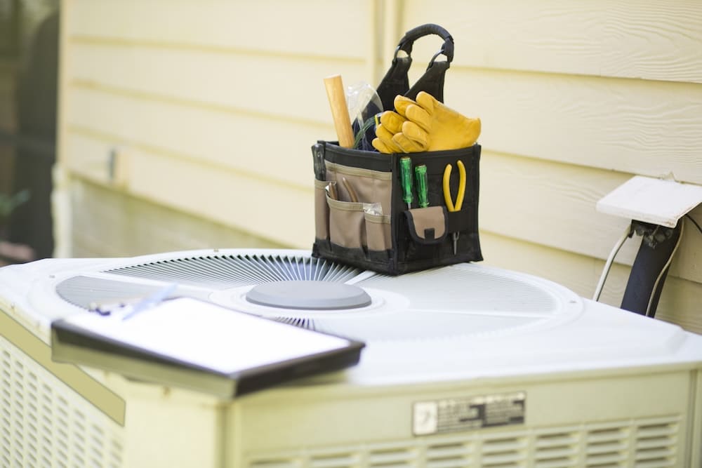 An outdoor air conditioning unit with toolbox and yellow gloves on top of it, indicating a technician is there to perform service