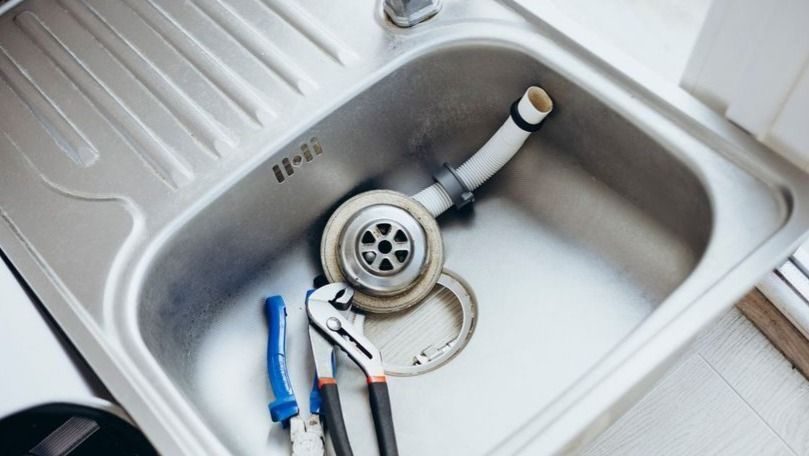 Stainless steel kitchen sink with a detached drain assembly and blue-handled pliers in the basin.