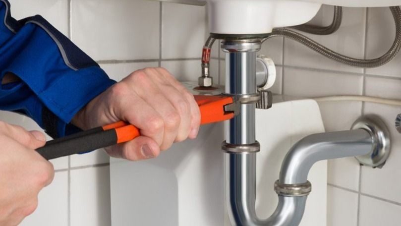 Close-up of hands using an orange-handled wrench to tighten the chrome P-trap under a sink.