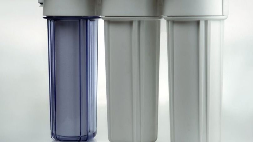 Three vertical water filter cartridges in a home filtration system, with a blue-tinted left cartridge and two white cartridges to the right.