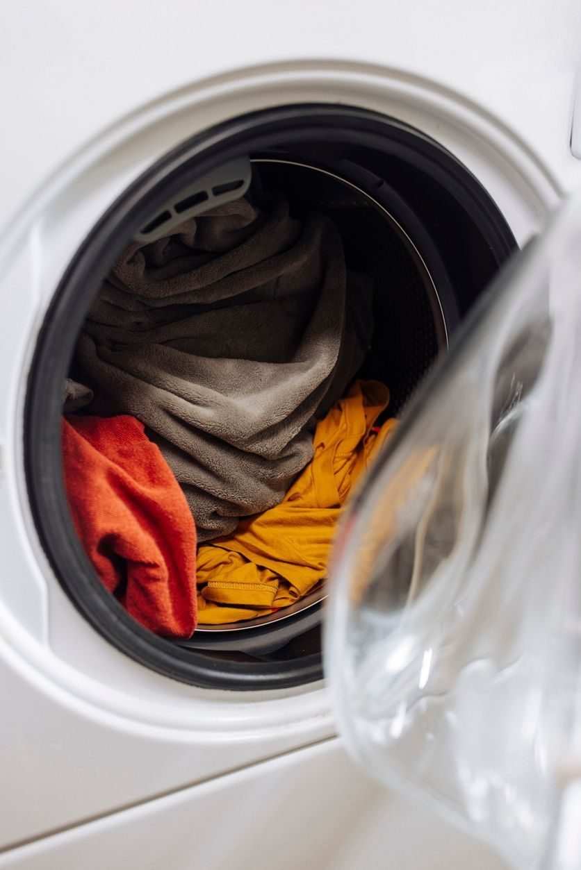 Open front-loading washing machine with mixed laundry inside, including a brown towel and an orange garment.
