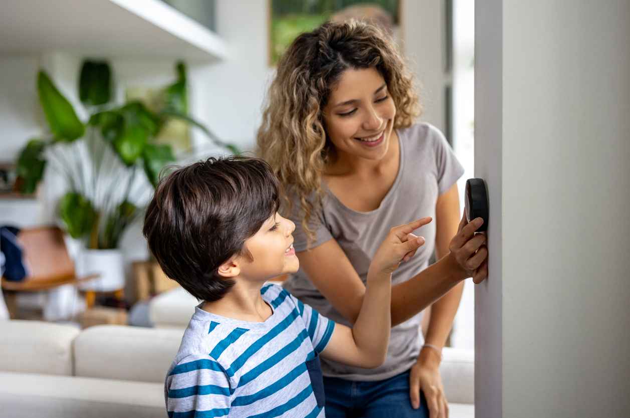 Happy mother and son at home using a smart thermostat to adjust the temperature.