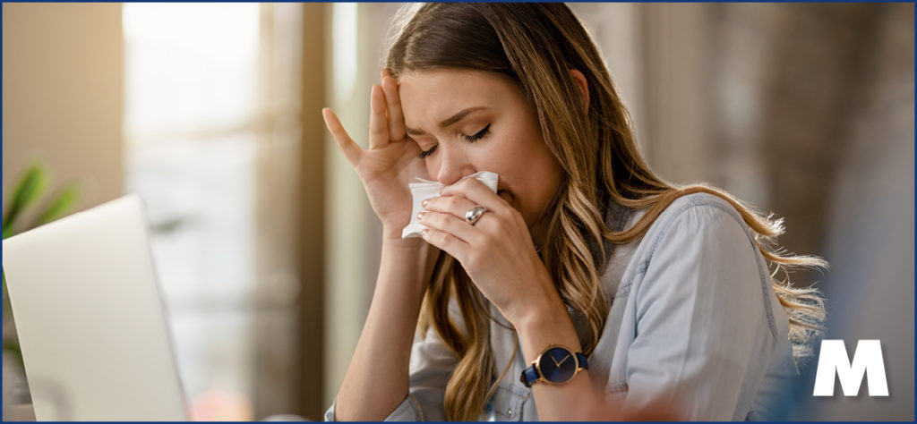 A woman with allergies sneezing into a tissue