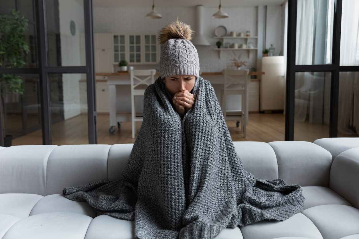 Adult woman sitting on the couch wrapped in a blanket due to heating problems