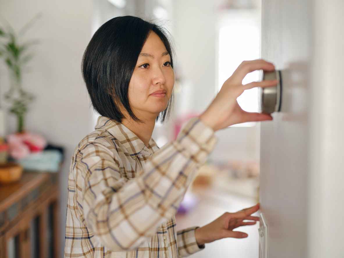 A woman in a home adjusting a smart thermostat.