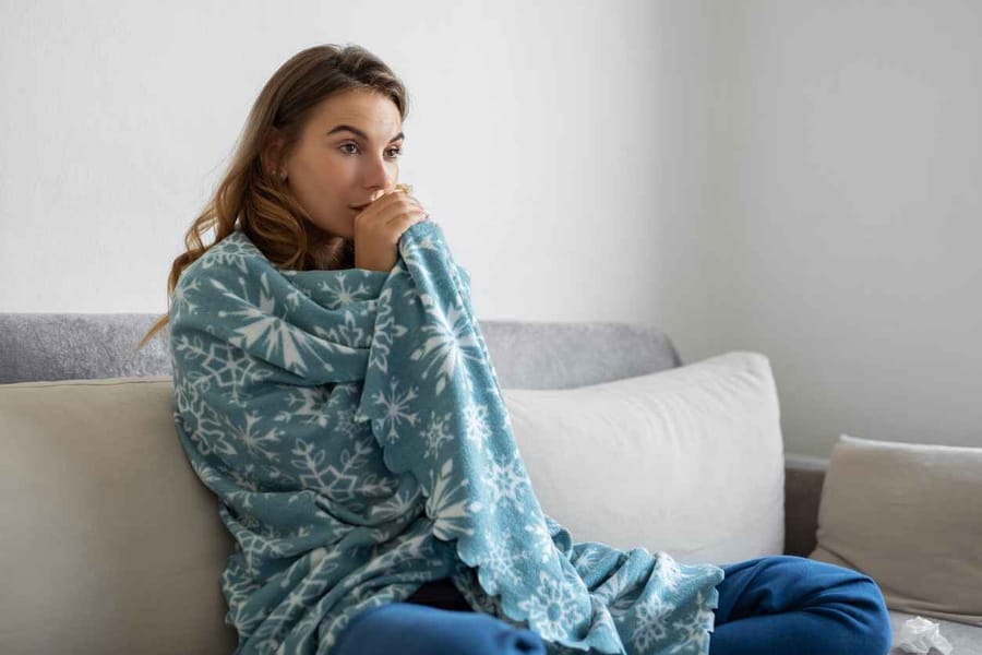 Woman sitting on her sofa with a blanket wrapped around her because her heater isn't working