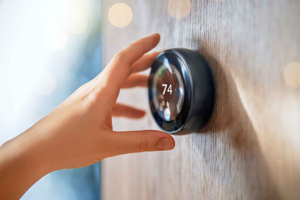 Hand reaching for the smart thermostat to adjust the thermostat