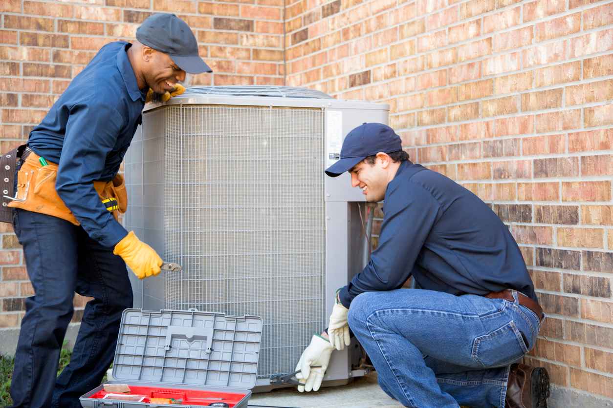 Team of two HVAC technicians installing an air conditioner. They prepare to begin work by gathering appropriate tools from their tool box.