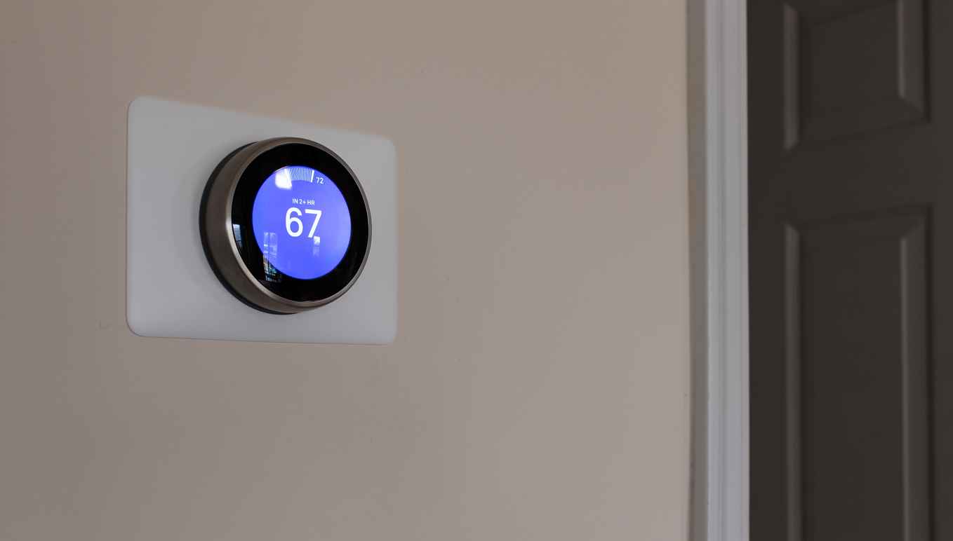 Smart thermostat on the wall of a residential home set to 67 degrees