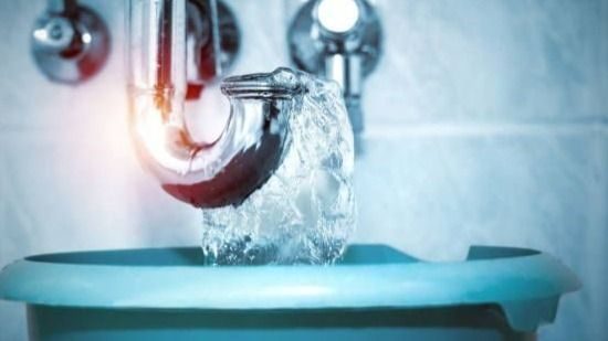 Close-up of a curved chrome faucet with water streaming into a blue sink basin.