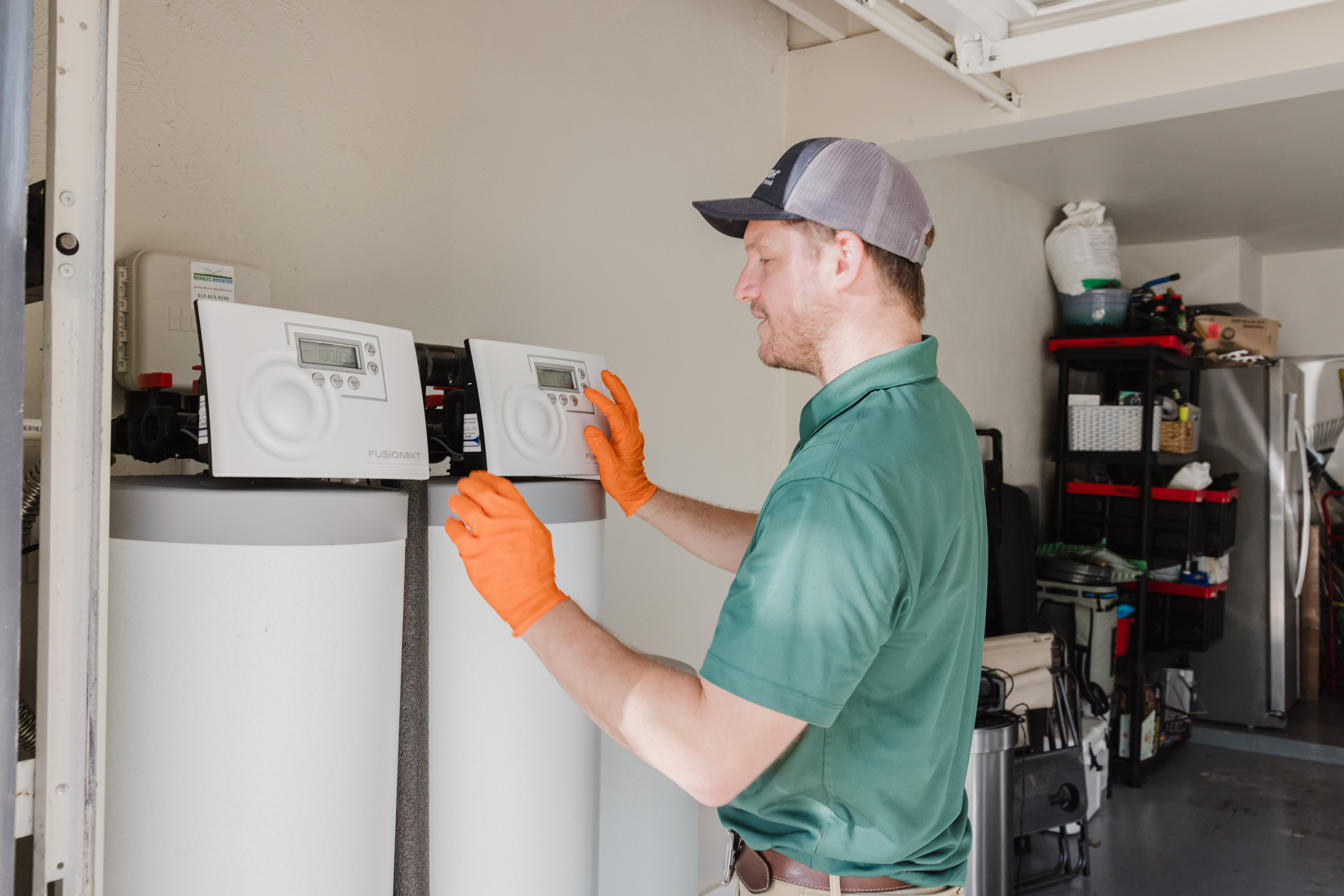 Maintenance technician in green shirt and orange gloves adjusts two white FusionNXT boilers in a utility room.