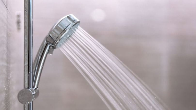 Chrome showerhead spraying water in a bathroom, close-up view.